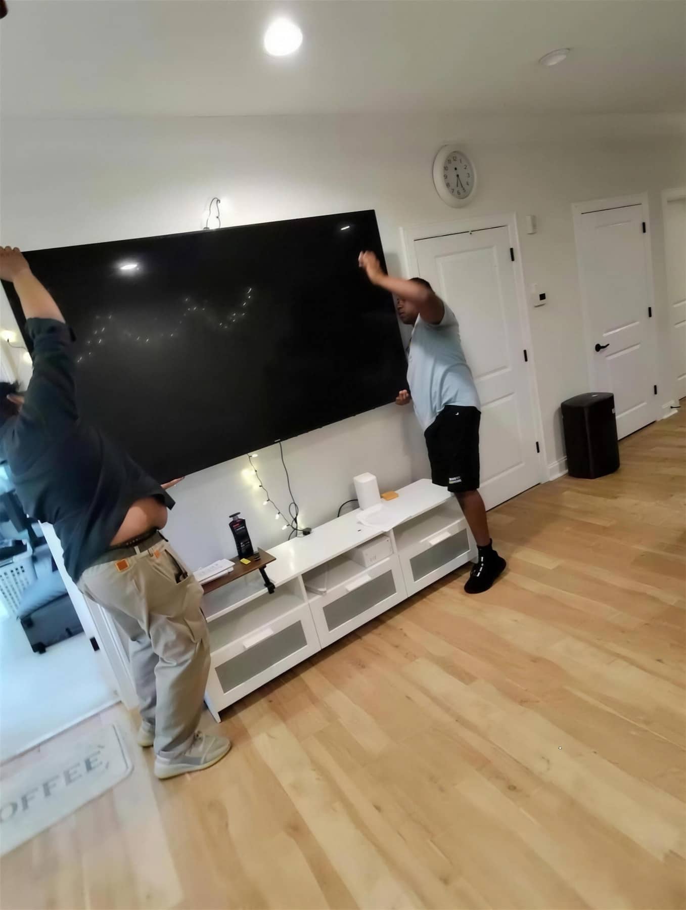 Two crew members carefully lowering a large flat-screen TV off its stand